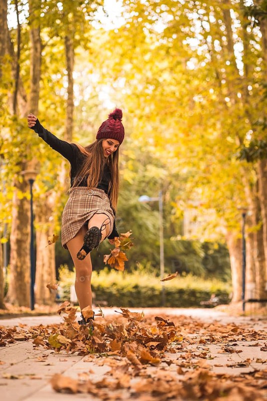 Portrait of a woman in autumn in a forest with brown leaves at sunset in a city park, kicking the leaves