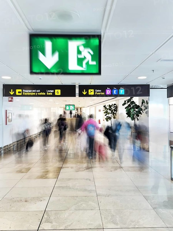 A dynamic scene captures the blurred motion of travelers in an airport corridor under signage, conveying energy, direction, and the fast pace of air travel environments