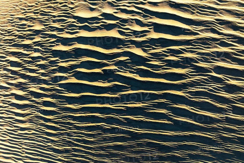 Aerial view of textured sand in La Puna desert, showcasing intricate patterns formed by natural elements. The sun casts shadows enhancing the captivating beauty