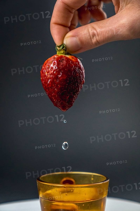 A nice water wet strawberry held by a woman's hand with black background