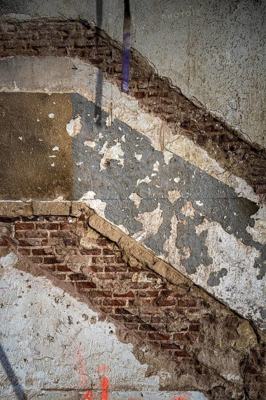 A close-up of an old wall under renovation, revealing layers of peeling plaster and exposed brick. The worn textures and faded paint highlight the passage of time and ongoing restoration efforts