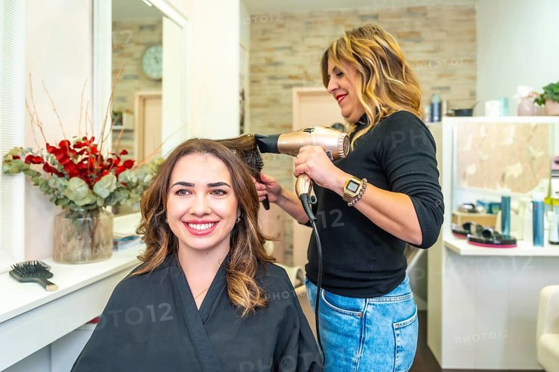 Happy client receiving a professional blow dry and hair styling treatment from a skilled hairdresser in a modern beauty salon, feeling refreshed and confident
