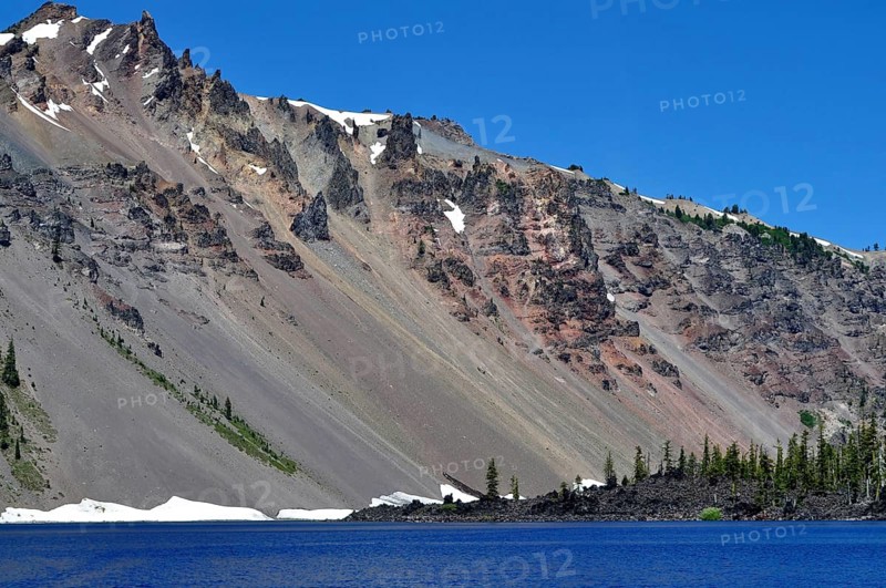 Mountain slope with snow and rock formations over a blue lake, Crater Lake National Park, Oregon, USA