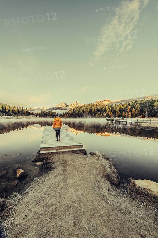 Young woman at Lake Staz near Sankt Moritz in the Engadine in Switzerland. Morning atmosphere with fog in autumn. Reflection of water