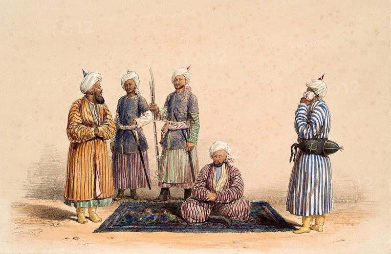 Five men in traditional clothing gather around a rug