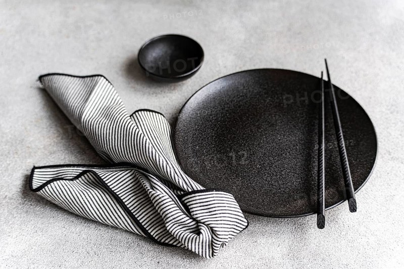 A sophisticated black and white table setting with a round black plate, chopsticks, and a striped napkin, presenting a minimalist and elegant dining theme