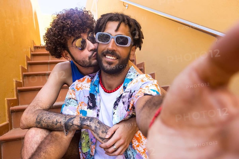 Two cheerful men, enjoying a bright summer day, share a close, intimate moment on a vibrant staircase, illustrating positivity and diversity in relationships