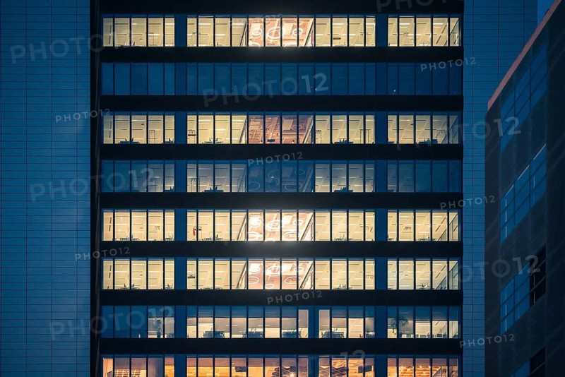 A modern office building illuminated from within as night falls. Rows of bright windows in a city center, showcasing business life and architecture in an urban setting