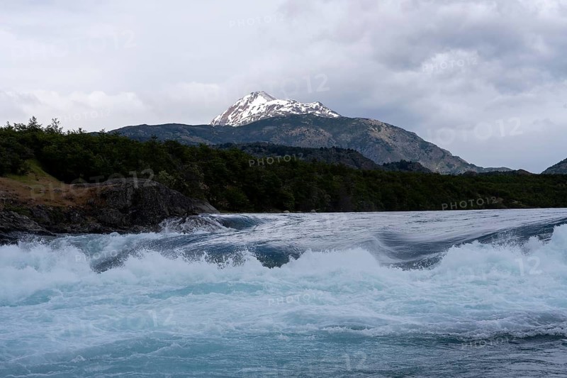 Rapids at the confluence of Río Baker and Río Neff, turquoise blue glacier water, snow-capped mountain peak in the background, cloudy sky, Aysén region, Chile