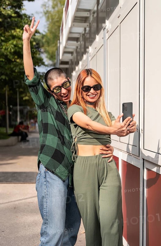 A cheerful Colombian lesbian couple takes a selfie together, smiling and posing playfully. Their stylish outfits, sunglasses, and relaxed energy reflect love, confidence, and joy in an urban setting