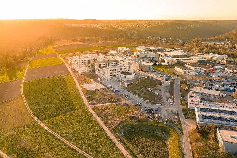 Industrial area and building complex in a hilly landscape photographed from the air at sunset, new hospital of the Verbund Südwest Clinic, Calw, Germany