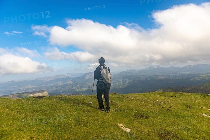 A woman is hiking through the scenic landscapes of Gorbea Natural Park in the Basque Country, Spain during autumn. She carries a backpack and walking stick, surrounded by vibrant fall foliage