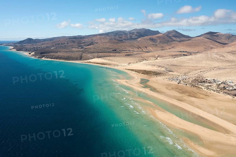 A breath-taking aerial view of Sotavento Beach in Fuerteventura, highlighting the turquoise waters juxtaposed against a golden coastline and rugged mountains