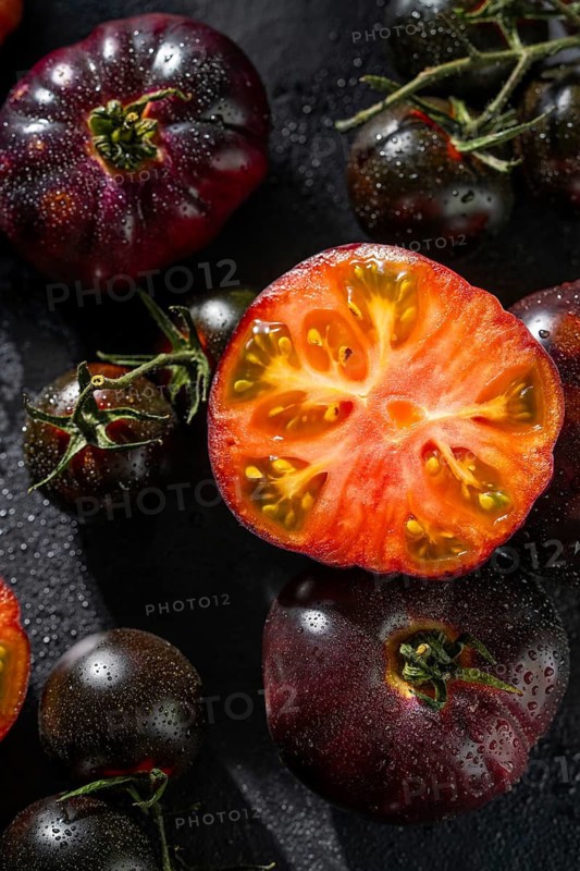 Close up of fresh black tomatoes with a vibrant red interior, glistening with water droplets. The dark surface accentuates the rich colors and textures of the tomatoes