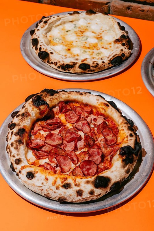 Wood-fired Four Meats pizza with smoked pork, salami, sausages, chicken, mozzarella, and tomato sauce, paired with Four Cheese pizza featuring parmesan, mozzarella, dorblu, and creamy sauce