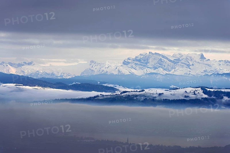 Fog over Lake Zug in the foreground the village of Cham, behind the snow-covered Alps with the Flübrig and Vrenelisgärtli mountains. Beinwil, Freiamt, Horben, Lindenberg, Canton of Aargau, Switzerland