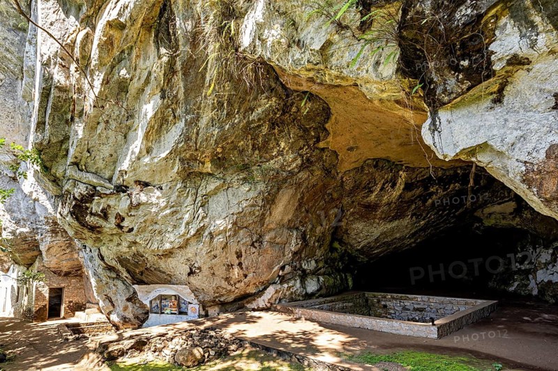 Large rock overhang with shady area, altar on the wall, The Batadombalena cave temple near Ratnapura in Sri Lanka