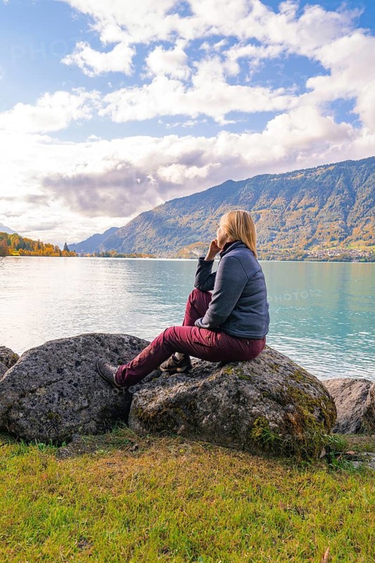 Woman sitting on rocks and looking at the lake with mountains in the background, Lake Brienz, Switzerland