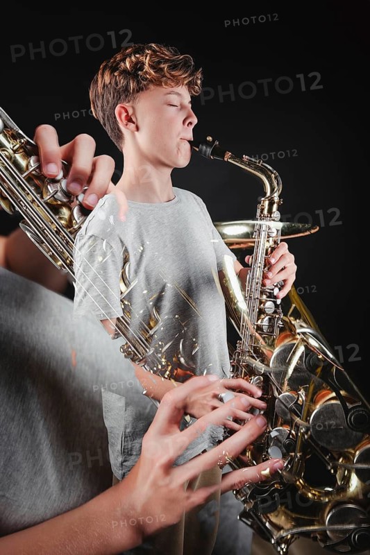 A teenage boy focuses intently as he plays a saxophone in a dark studio setting, highlighting his passion and skill in music