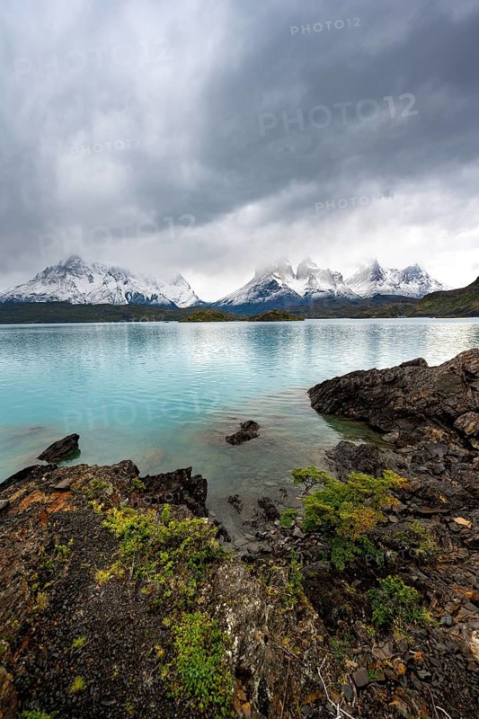 Cloudy mountain range Cuernos del Paine, shore of the blue lake Lago Pehoe in the evening light, dramatic sky, Torres del Paine National Park, Chile