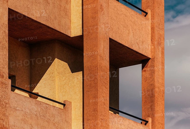 Modern architectural facade featuring geometric patterns and warm, textured surfaces. The play of light and shadow adds depth and highlights the building's distinct lines