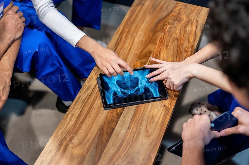 Healthcare professionals in scrubs are analyzing a hip and pelvis x ray image on a digital tablet, pointing and discussing, emphasizing modern medical collaboration and teamwork