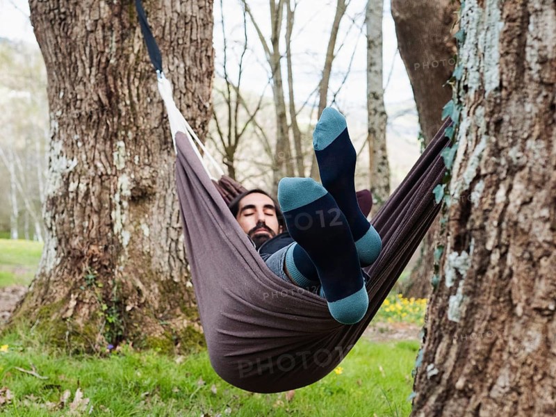 A man peacefully rests in a hammock suspended between trees in a serene forest setting. Surrounded by nature, he enjoys tranquility, illustrating a perfect escape from everyday life