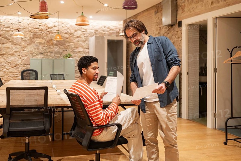 Two colleagues collaborate in a cozy coworking space with a rustic design. They discuss documents, illustrating teamwork and productivity in a modern office environment