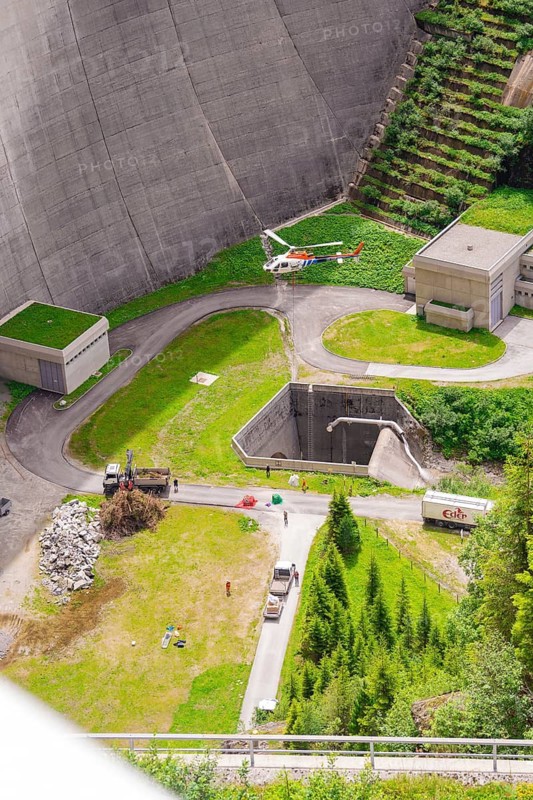 View from above of a dam with buildings and a helicopter surrounded by green trees, Klein Tibet, Zillertal, Austria