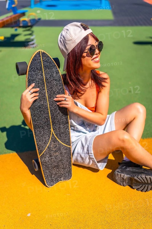 Vertical Portrait of a modern young woman with skateboard in a park with colorful ground