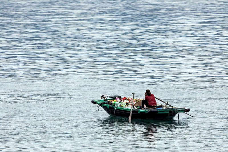 A person sits in a small boat on a calm lake surrounded by blue water, woman in a rowing boat in Halong Bay in Vietnam