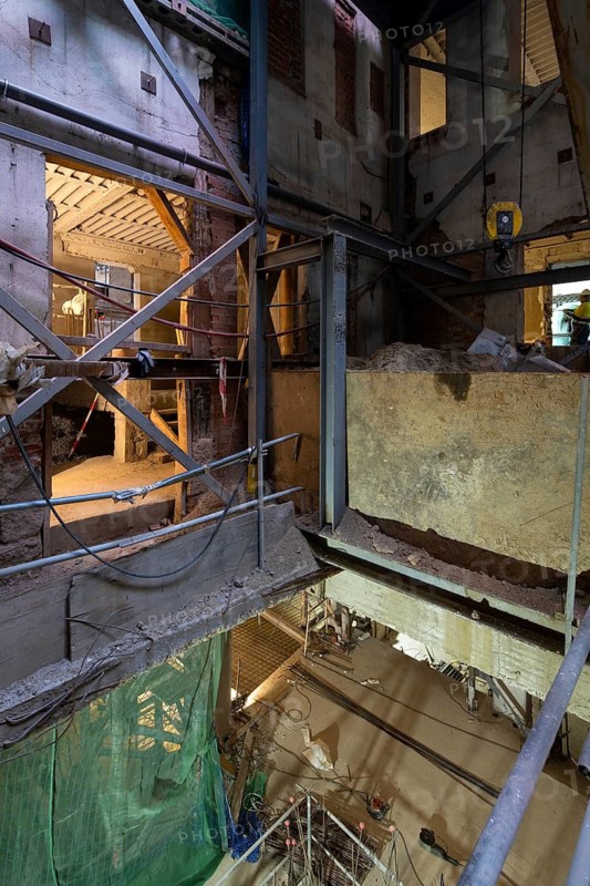 An indoor construction site with metal beams, scaffolding, and workers. The dim lighting highlights the structure's rough textures and ongoing work