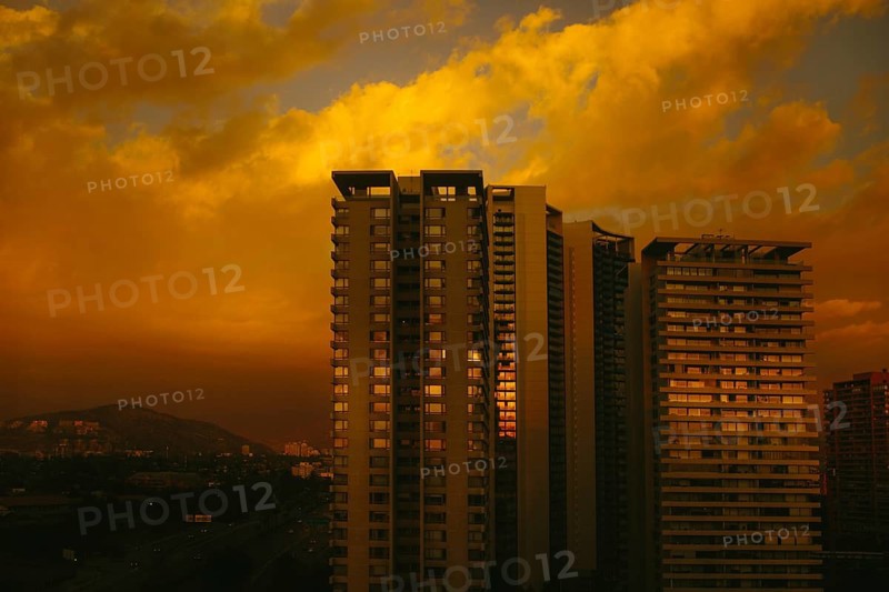 An atmospheric twilight encompassing high-rise apartment buildings. The fading sunlight casts a dramatic golden-orange hue across the scene, evoking an urban sunset over the expansive skyline