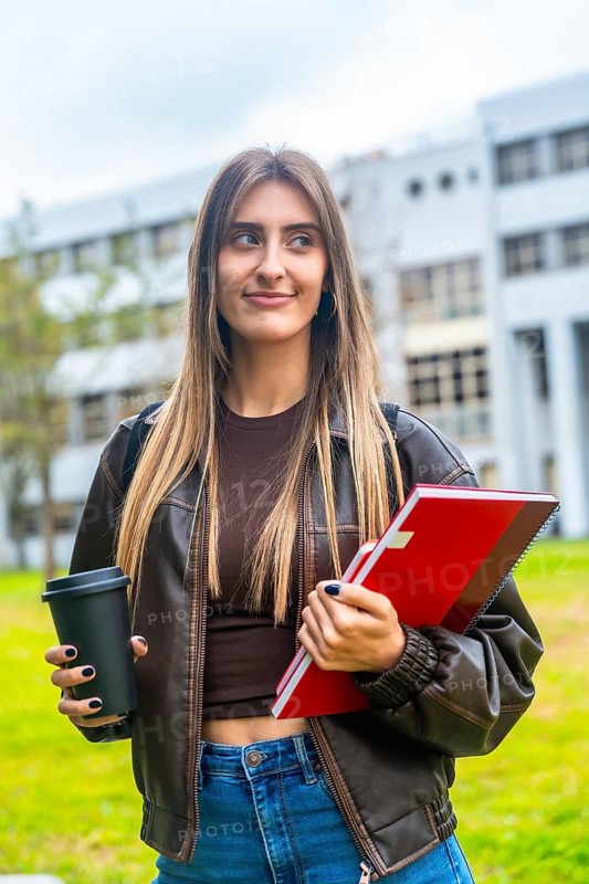 Young female student on campus holding coffee and notebooks, dressed casually in brown jacket and jeans, focused and ready for study, planning future academic goals and success