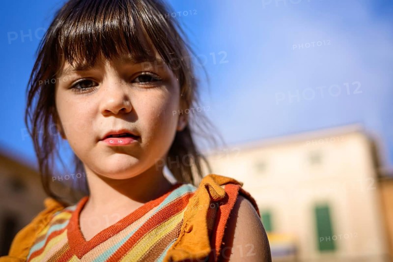 Close up of a young girl with bangs standing outdoors on hockey day. The bright sunlight highlights her expressive eyes and lips against a clear blue sky background