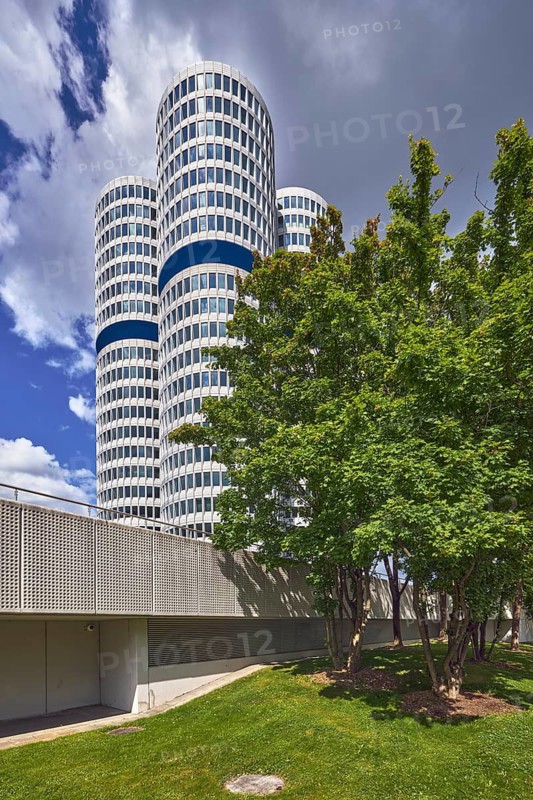 BMW group headquarters, BMW four-cylinder engine, BMW tower, BMW high-rise building, architect Karl Schwanzer, commercial building, high-rise building, modern architecture, trees, meadow, overcast sky with a little blue, dark gray cumulus clouds, Petuelring, Munich, state capital, district-free city, Bavaria, Germany