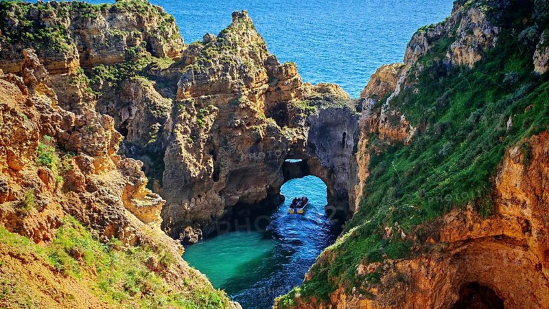 Impressive cave and rock formations with a boat with tourists exploring the coastline, Ponta da Piedade, Lagos, Algarve, Portugal
