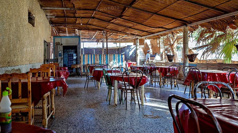 A cosy restaurant with a wooden roof and groups of tables under natural light in a relaxed atmosphere, restaurant in a village in the Sahara in Algeria