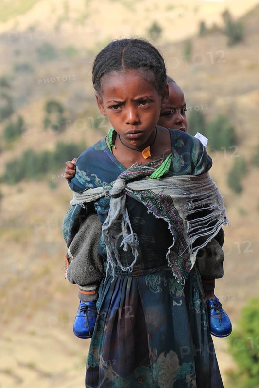In the highlands between Mekele and Lalibela, girl carries sibling on her back, Ethiopia