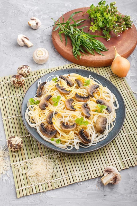 Rice noodles with champignons mushrooms, egg sauce and oregano on blue ceramic plate on a gray concrete background. side view, close up