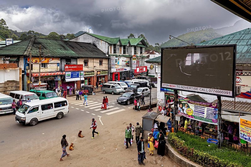 Lively road junction with traffic and billboards against a mountainous backdrop, Nuwara Eliya Sri Lanka Bus Station