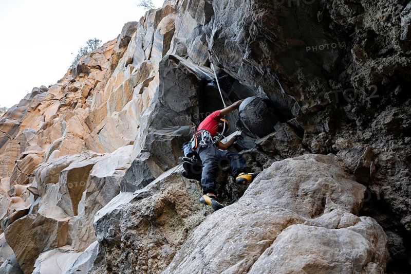 A climber expertly navigates a rugged rock face, showcasing skill and determination in traditional climbing. The natural setting emphasizes the adventurous spirit of the sport