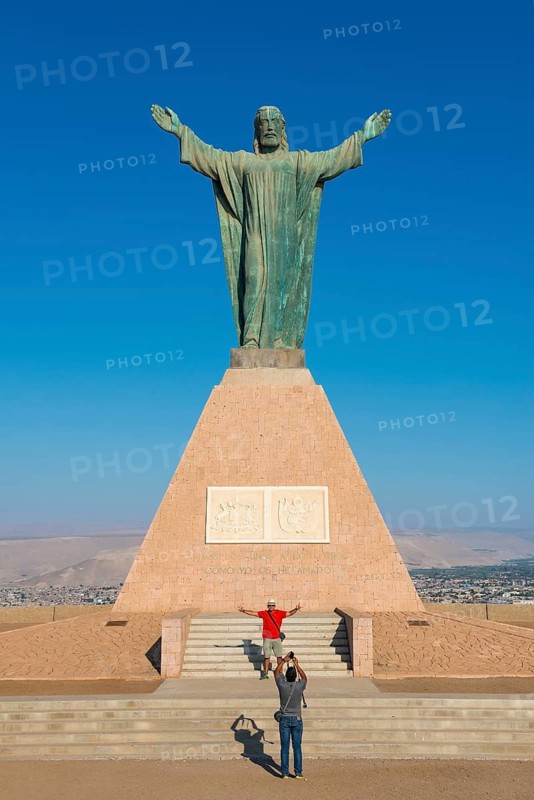 Tourists taking photos in front of the large statue of Christ on the Morro de Arica lookout mountain, city of Arica, Chile