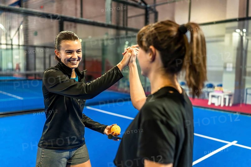 Female athletes sharing a supportive high five gesture after playing a pickleball match on an indoor court, celebrating teamwork, good sportsmanship, and success during recreational activity