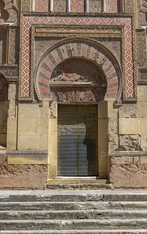 Cathedral Mosque of Córdoba, Mezquita-Cathedral, A magnificent Islamic archway full of ornamentation and patterns surrounded by stone structures, An ornately decorated Islamic-style door with decorative patterns stands on a series of stone steps, Cordoba, Andalusia, Spain