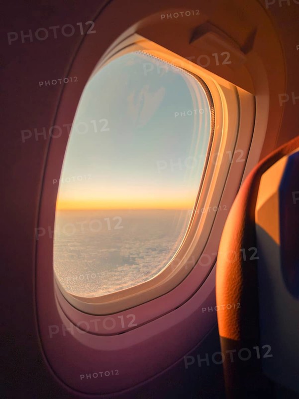 Warm sunset hues fill the sky as seen through the window of an airplane, highlighting the silhouette of the aircraft's interior