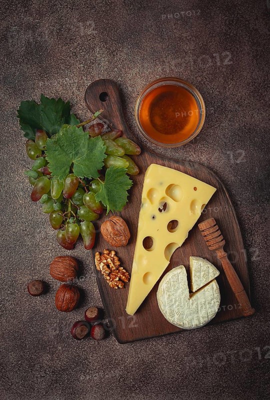 Cheese with big holes, emmental, maasdam, brie cheese, on a cutting board, with grapes and honey, nuts, appetizer to wine, top view