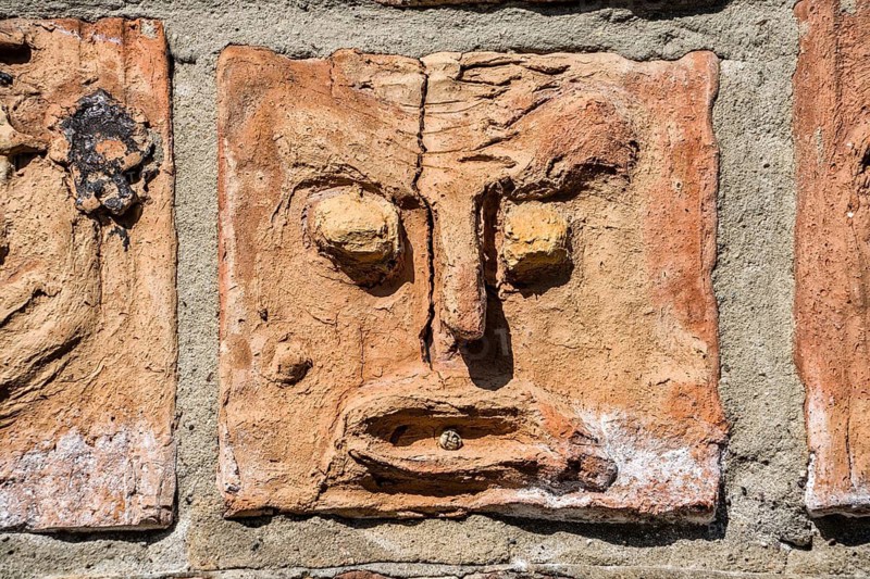 Artistic installation with mask and facial reliefs made of terracotta, in a historic brick wall, Warburg, North Rhine-Westphalia, Germany