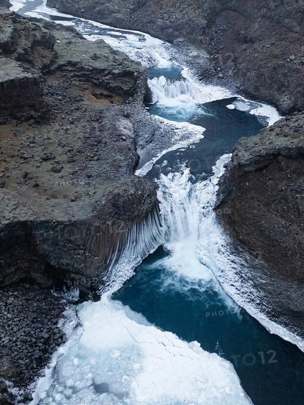 Aerial view of a breathtaking Icelandic winter landscape showcasing a majestic frozen waterfall cutting through rugged terrain, highlighting the wild beauty of nature