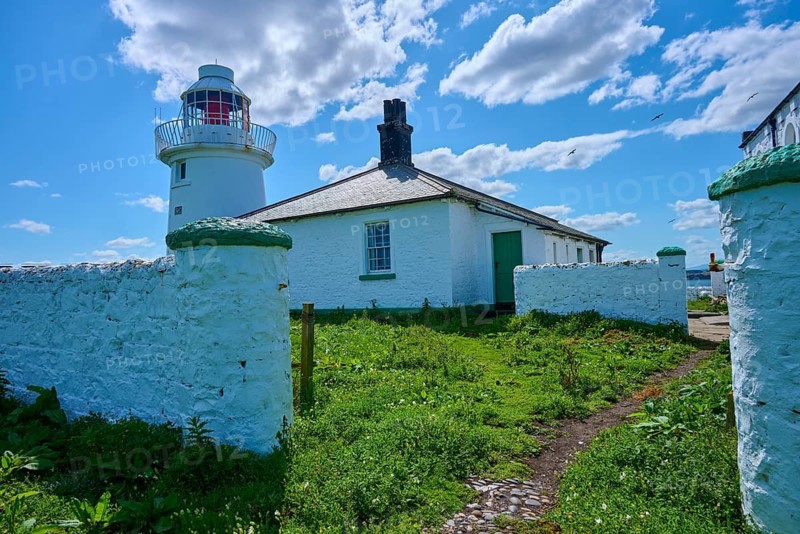 White lighthouse next to green garden and historic house under sunny sky, Inner Farne Lighthouse, Seahouses, Inner Farne, Ferne Islands, Northumberland, England, Great Britain
